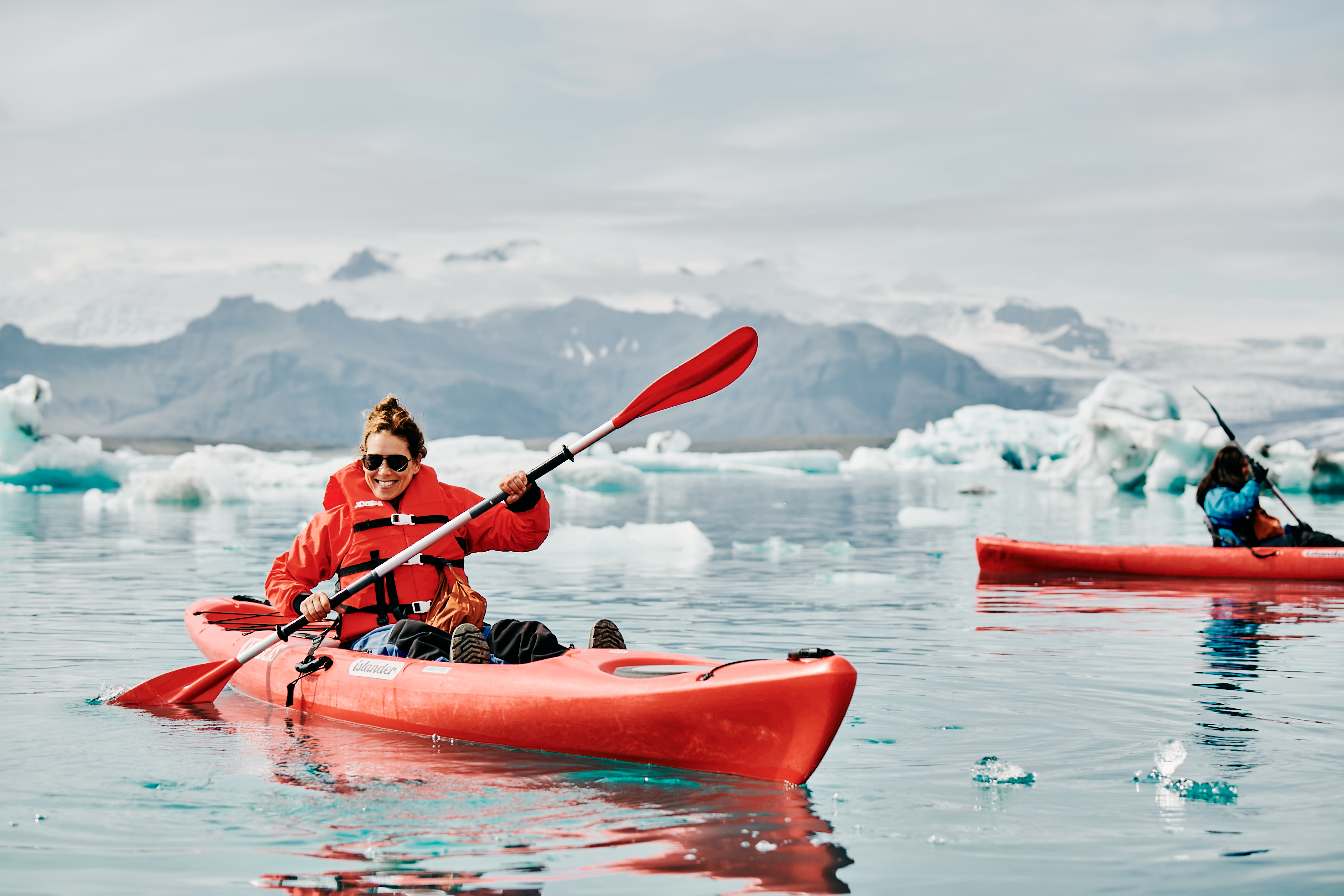 a woman paddles a red kayak in Glacier Lagoon in Iceland.