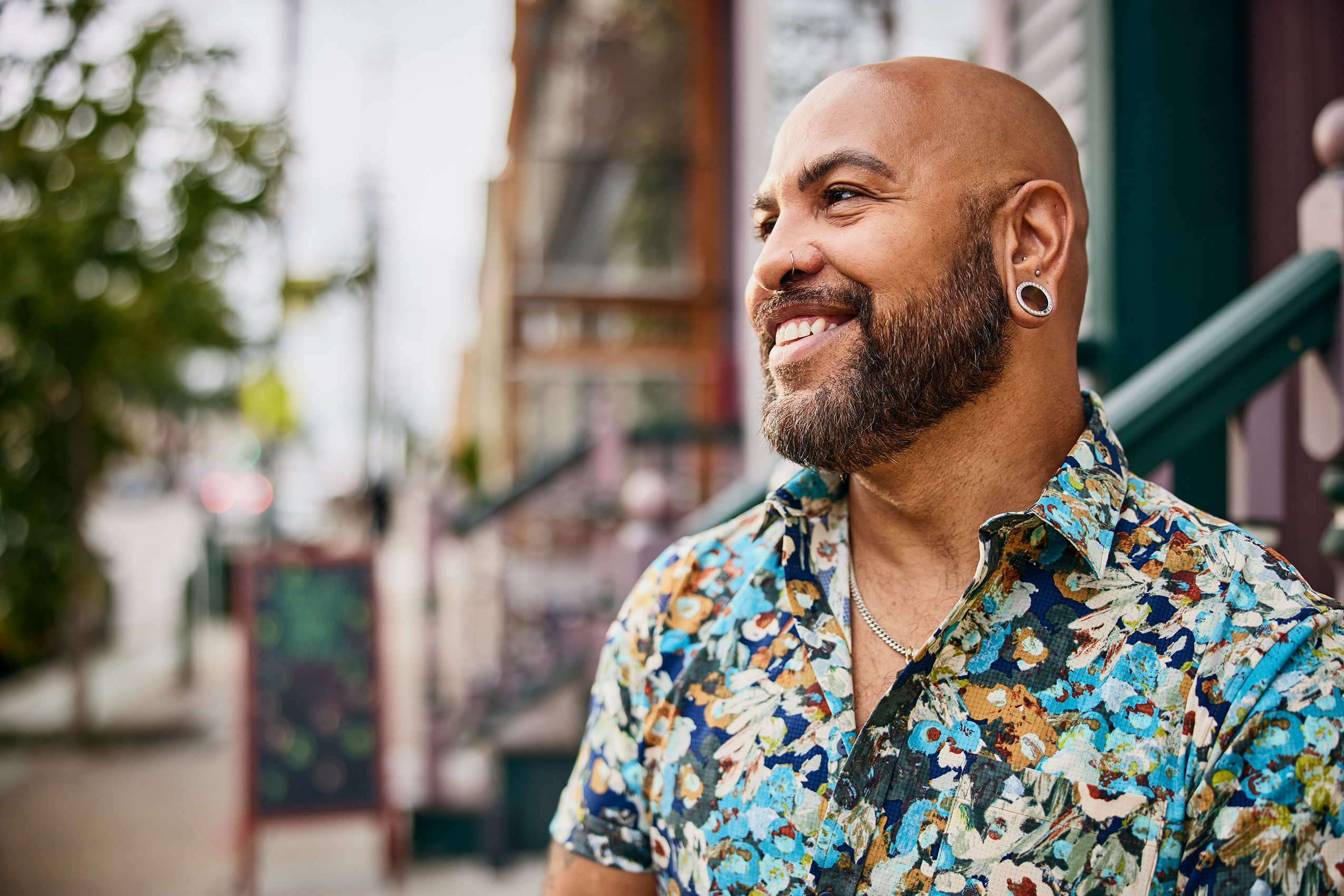 man smiles outside of coffee shop wearing a colorful shirt