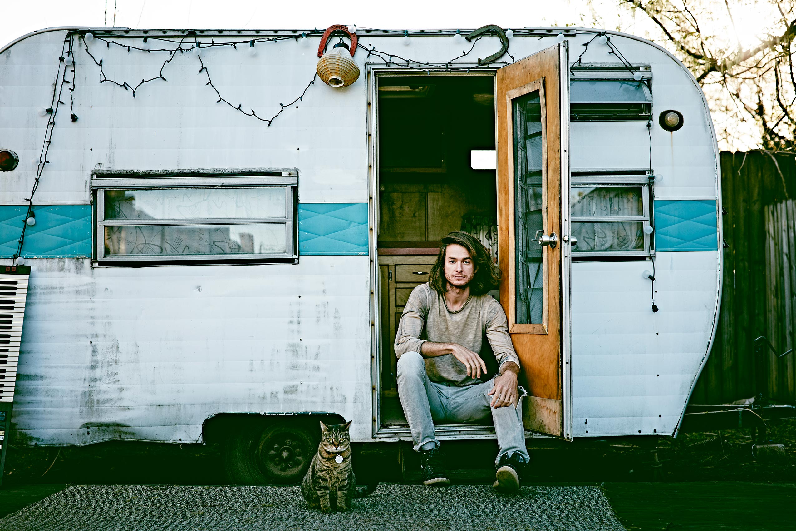 a man sits in front of his vintage camper with a cat