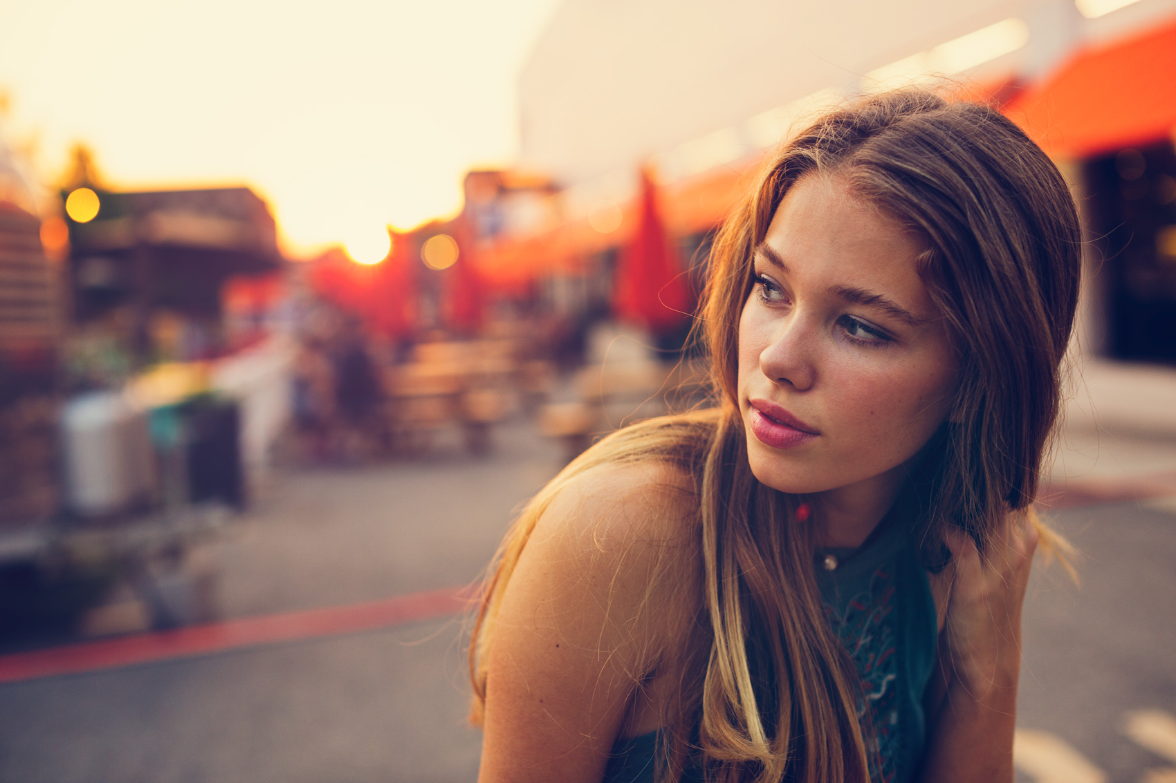 A young woman poses for a portrait at a market at sunset.