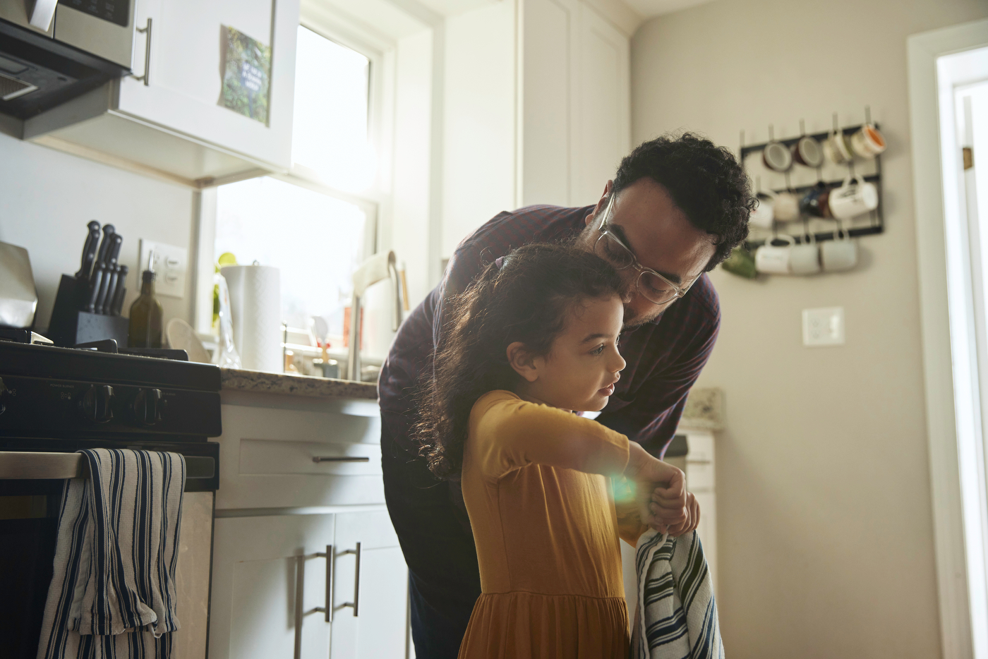 A father kisses his daughter on her head in their kitchen.