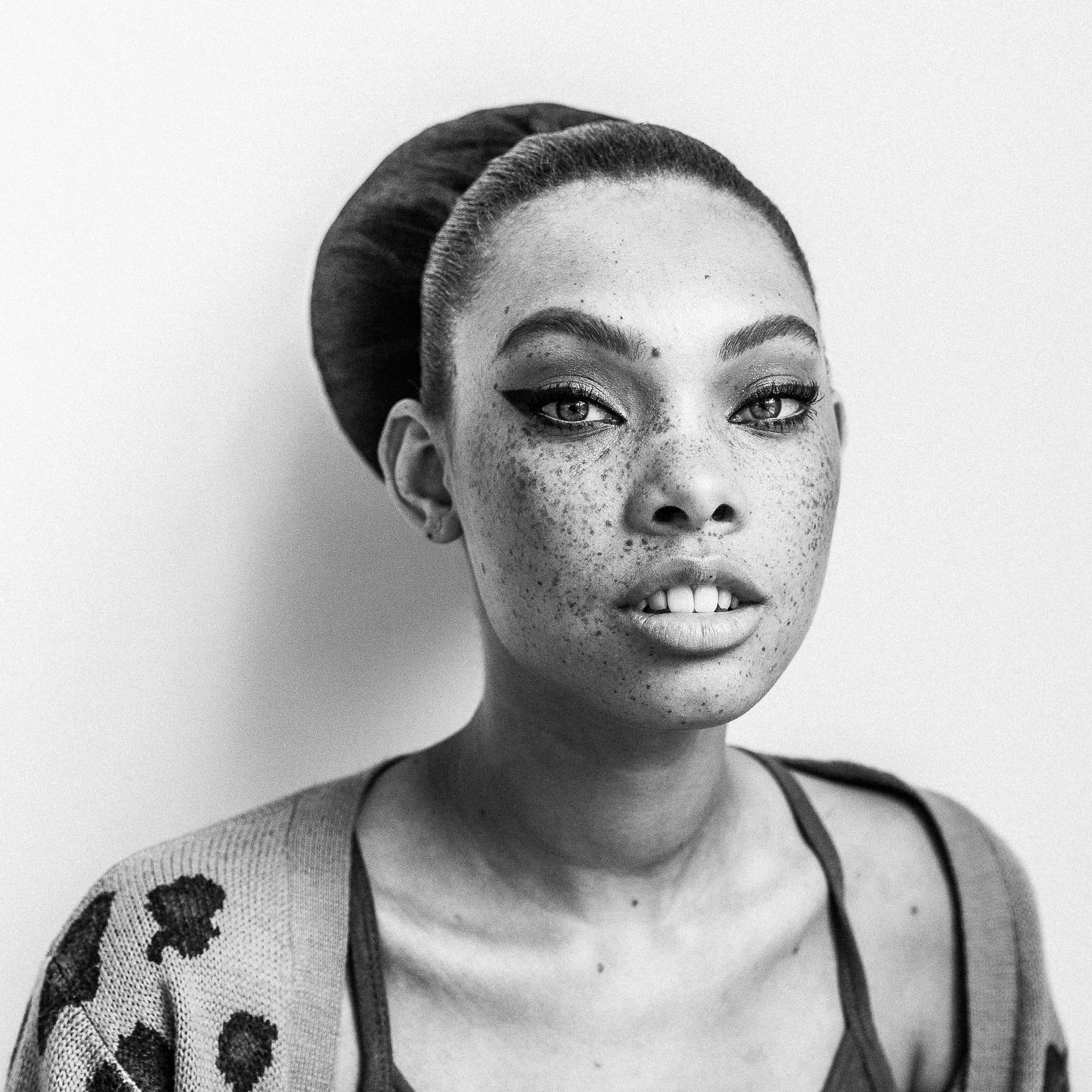 Portrait outtake of young freckled woman against white wall. 