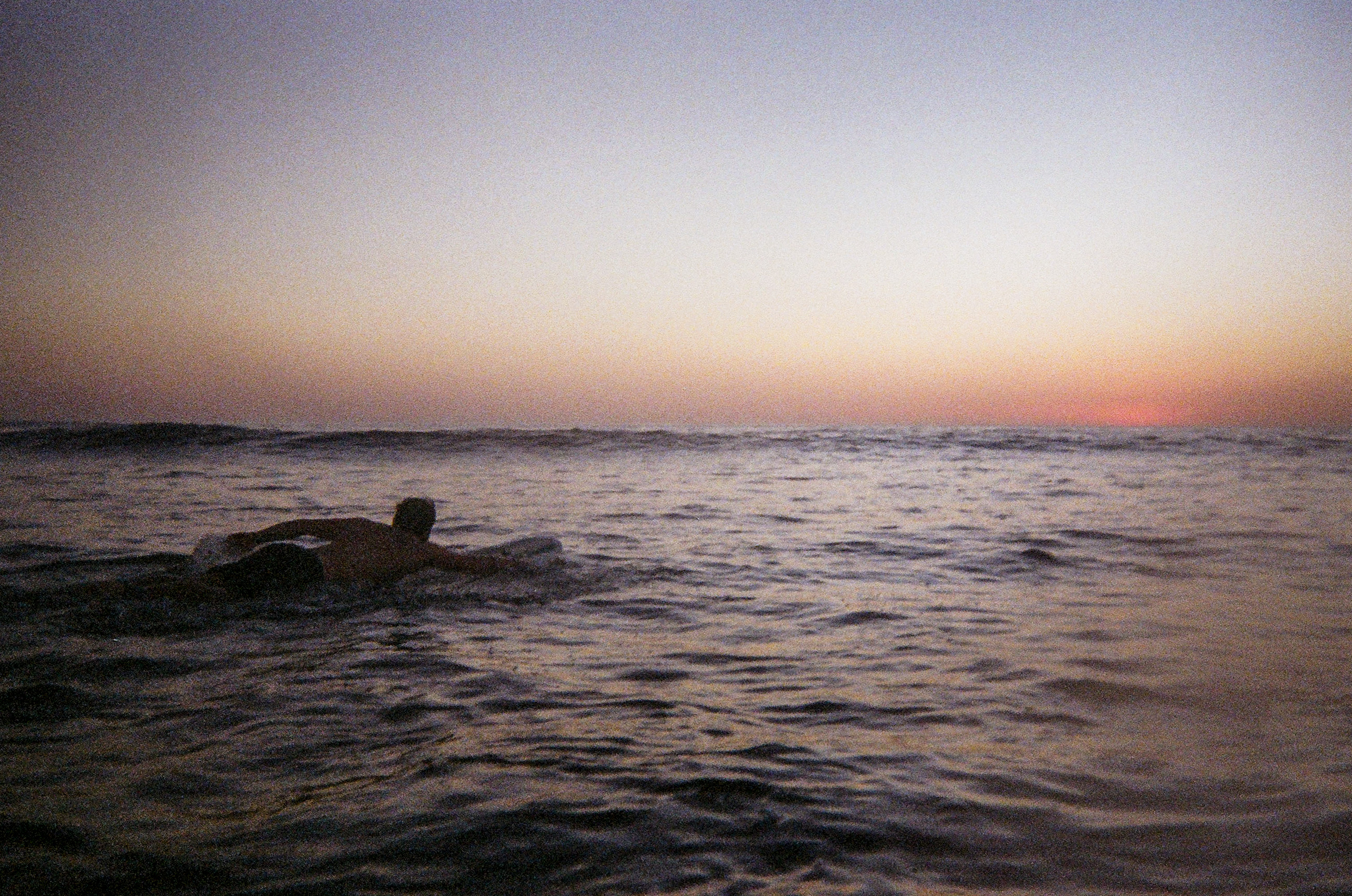 A surfer heads out at sunset to surf in Nosara Costa Rica where surfing is a tourist attraction. 