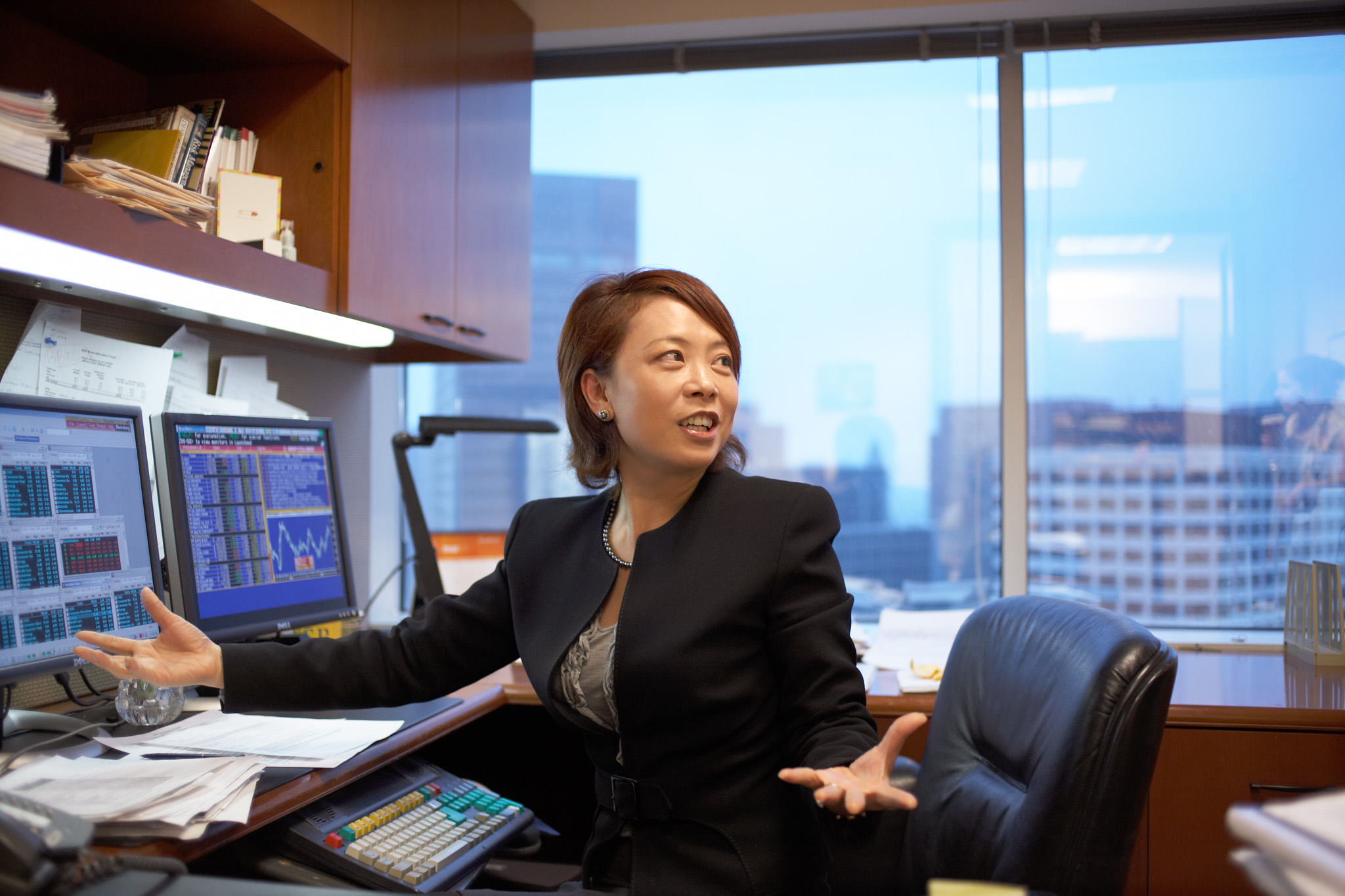 Financial analyst working in front of multiple computer screens, talking with co-worker.