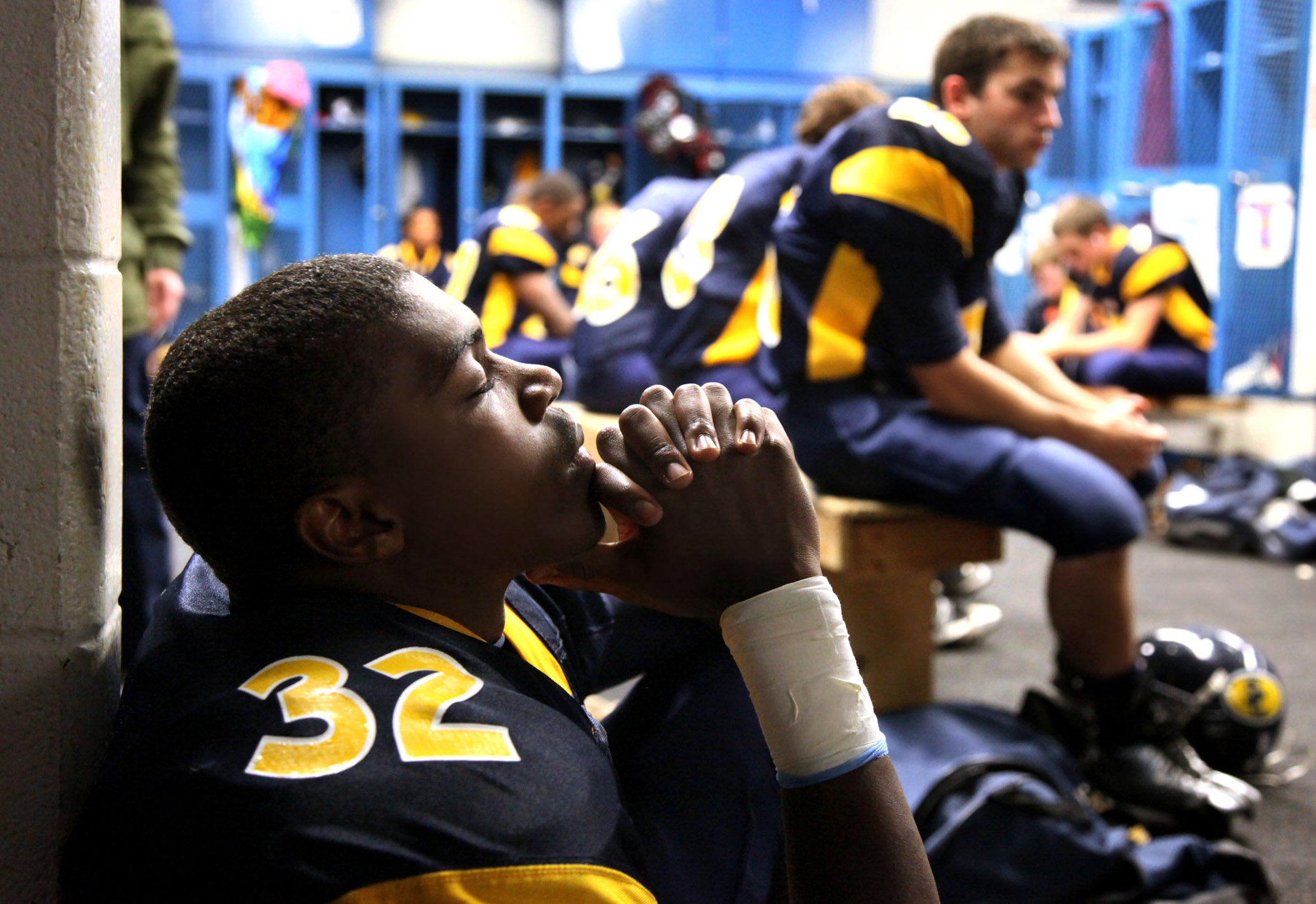A football player prays in the locker room before the start of a friday night high school football game.