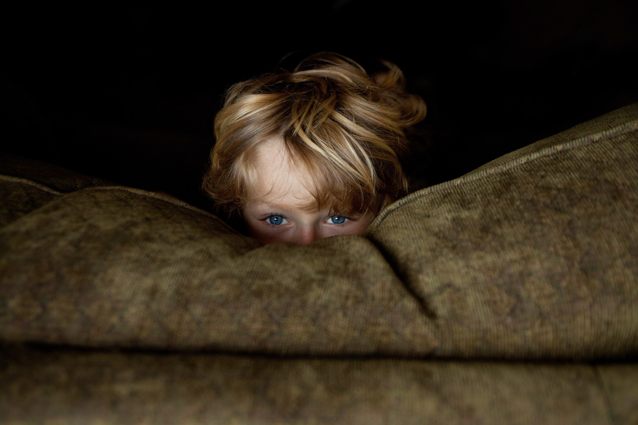 A boy looks from behind the couch at his home in Southern California.