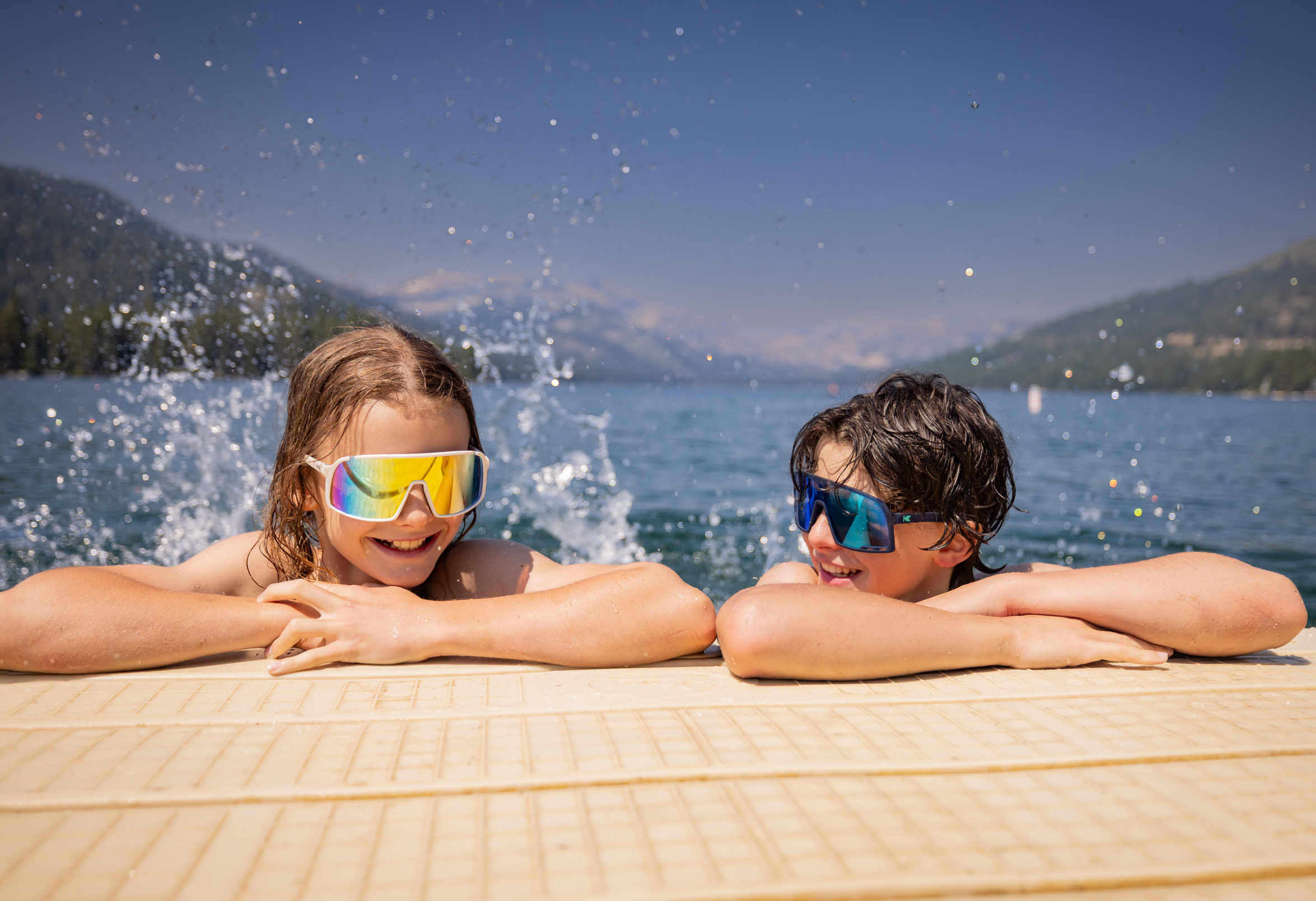 Friends share a carefree swim with mirrored shades reflecting the bright alpine sky.