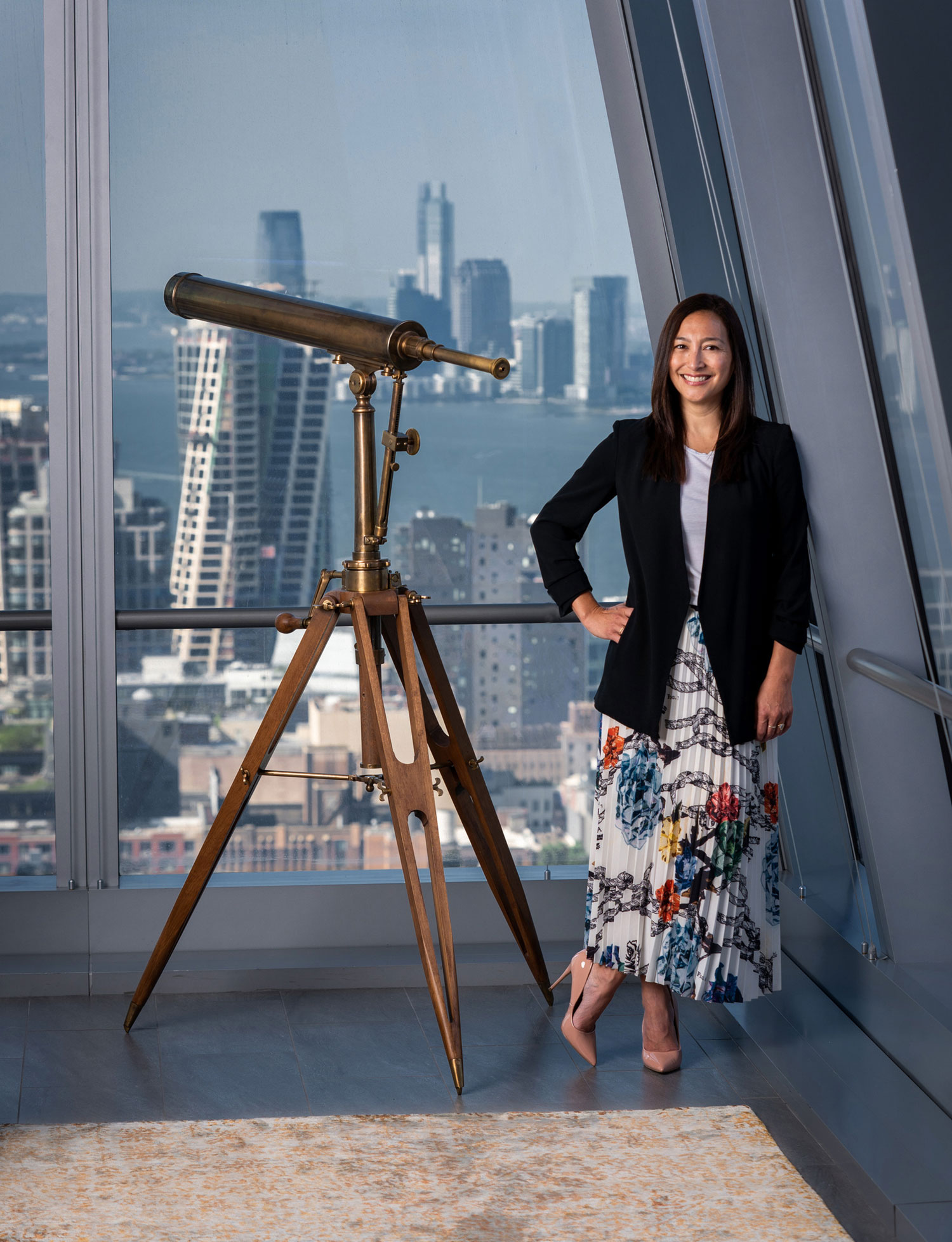 Environmental portrait of woman in her office with cityscape view in the background.